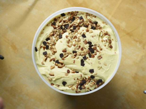 Overhead view of a large tub of vanilla chocolate chip almond ice cream on a yellow background