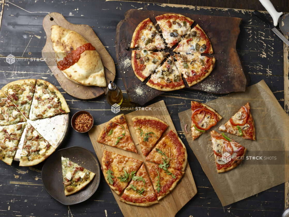 Various sliced pizzas overhead on wooden boards with a panzerotti