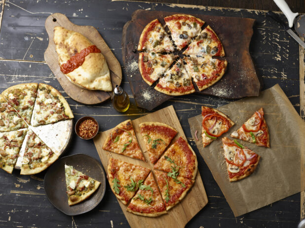 Various sliced pizzas overhead on wooden boards with a panzerotti