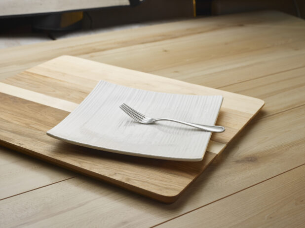 A fork on a square white plate sitting on a wooden cutting board