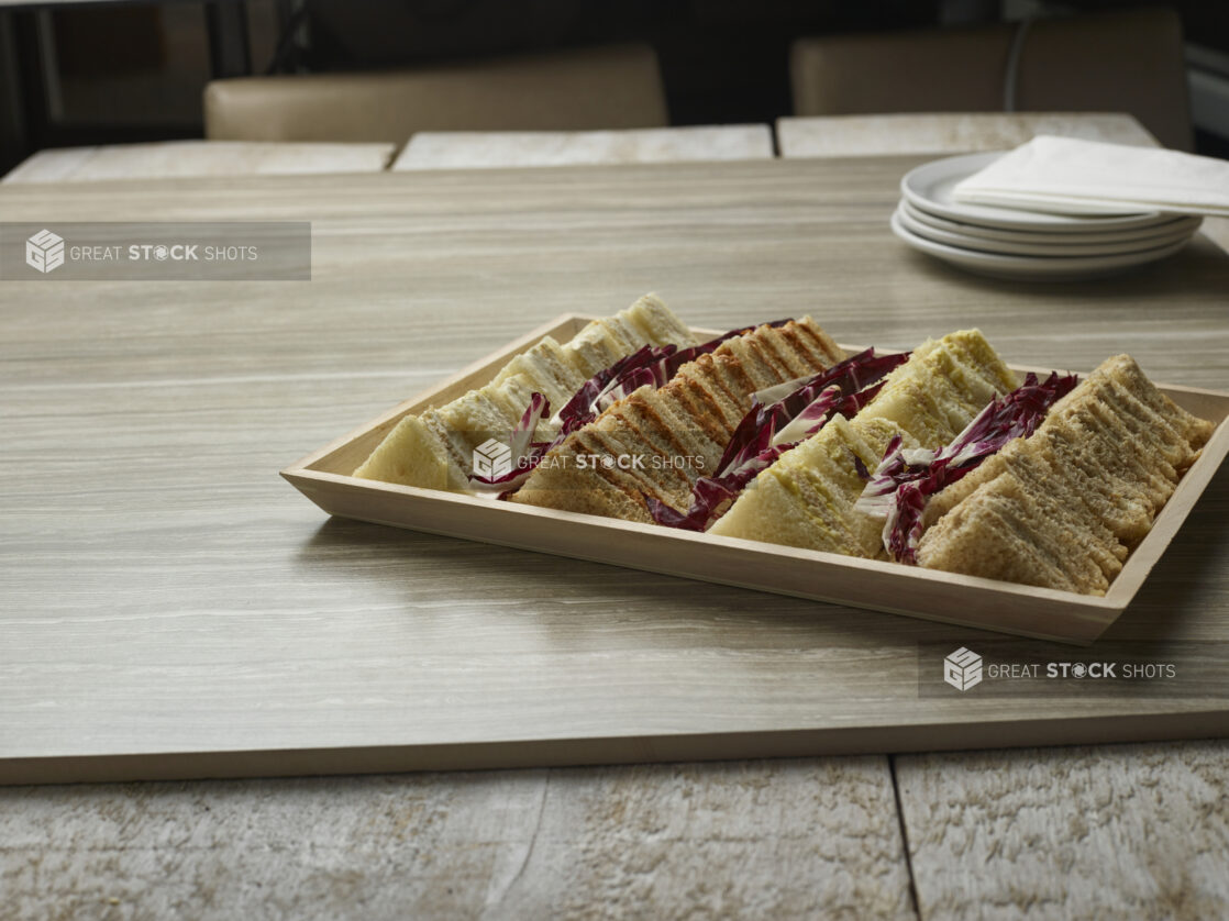 A variety of finger sandwiches on a wooden tray on a wooden background