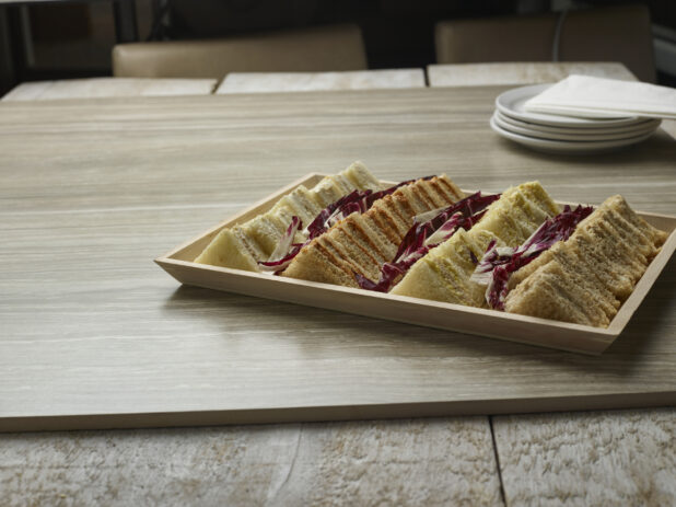 A variety of finger sandwiches on a wooden tray on a wooden background