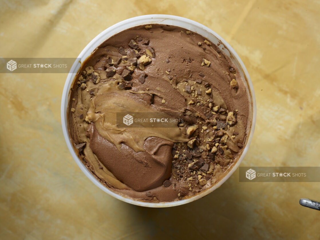 Overhead view of a large tub of chocolate peanut butter swirl ice cream on a yellow background