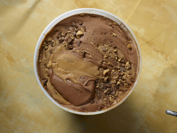 Overhead view of a large tub of chocolate peanut butter swirl ice cream on a yellow background