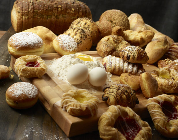 Collection of various breads and pastries with fresh eggs and flour with an egg well on a wooden block