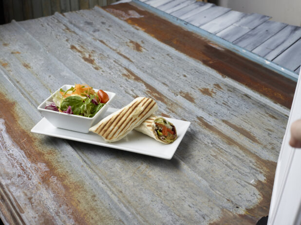 Grilled vegetable wrap cut in half with a side garden salad on a rustic corrugated metal background