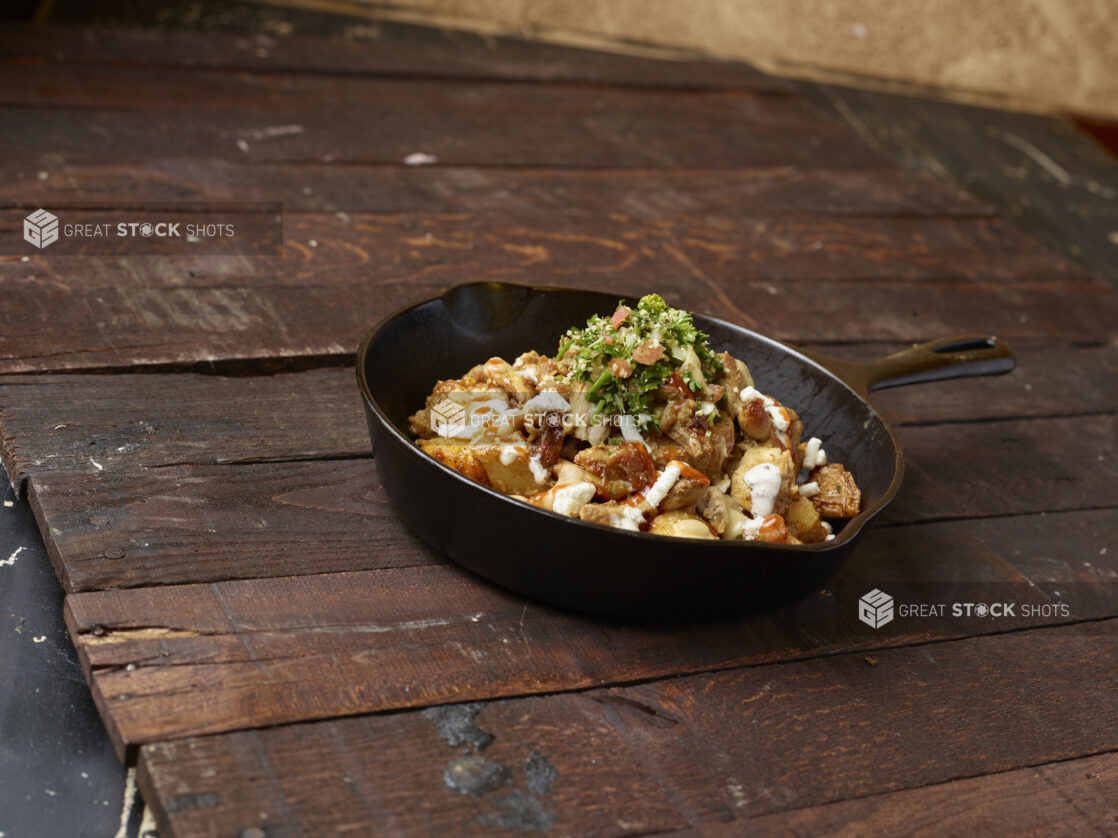 Black iron skillet with chicken kebab, potatoes and tabouli, drizzled with white sauce on a wooden background