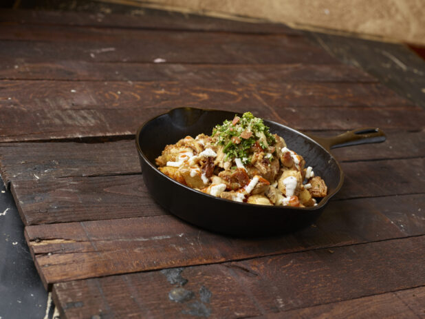Black iron skillet with chicken kebab, potatoes and tabouli, drizzled with white sauce on a wooden background