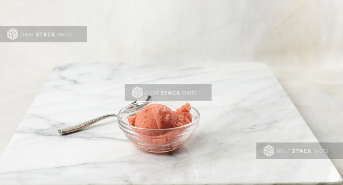 Glass bowl of strawberry gelato on a marble background