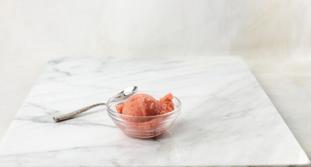 Glass bowl of strawberry gelato on a marble background