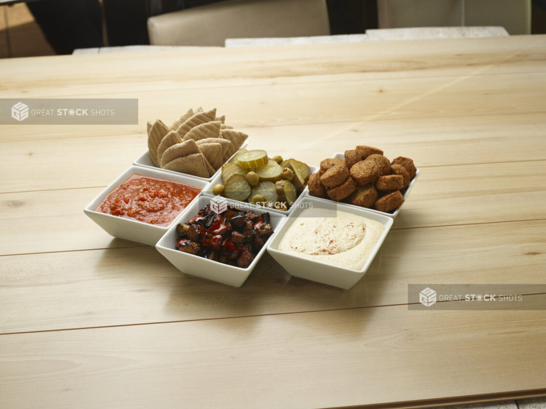 Various small white bowls of food and dips on a wooden background