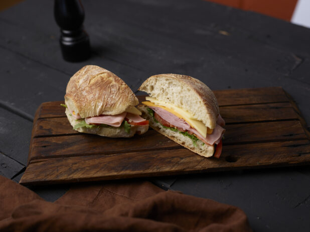 Ham and cheese sandwich on a crusty bun on a wooden board on a dark background