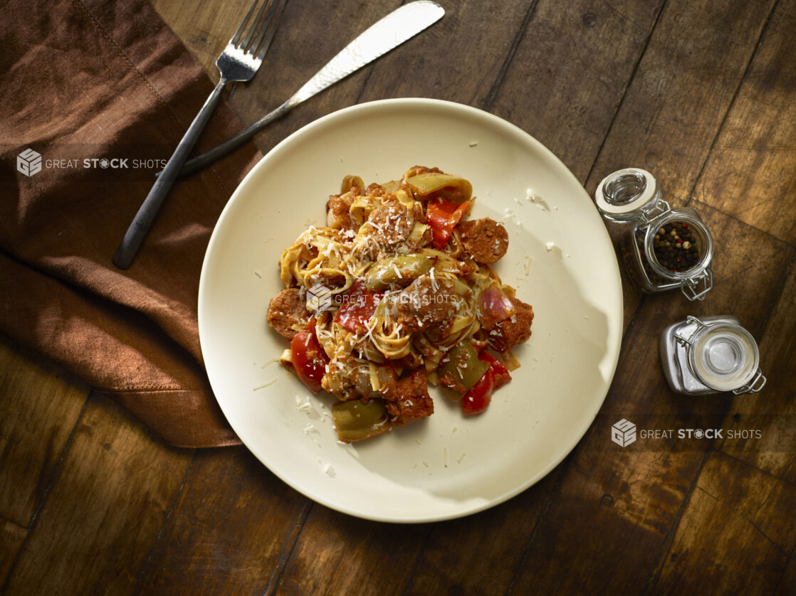 Overhead of sausage and bell pepper fettuccini on a white plate with a dark wooden background