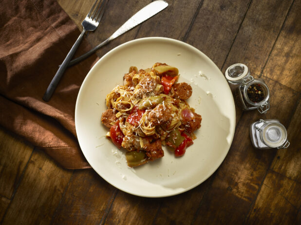 Overhead of sausage and bell pepper fettuccini on a white plate with a dark wooden background