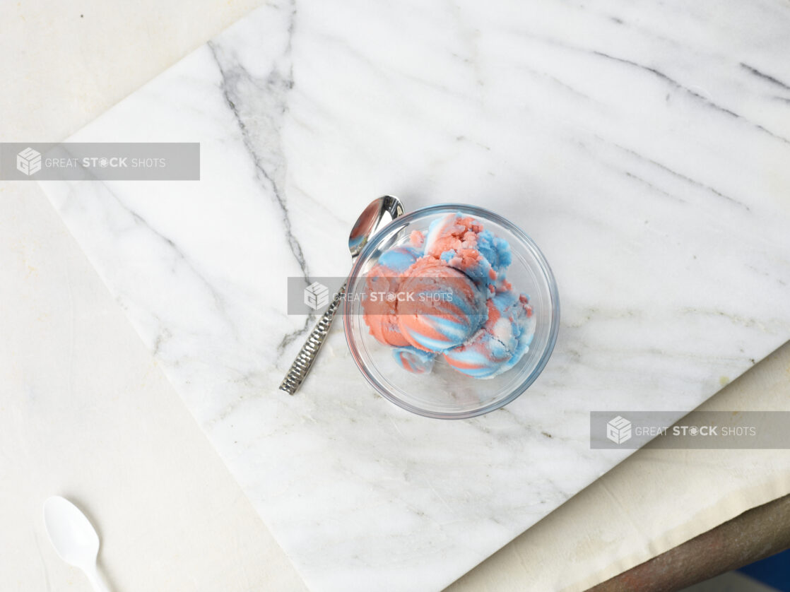 Multicolored gelato in a glass bowl with spoon on a marble background