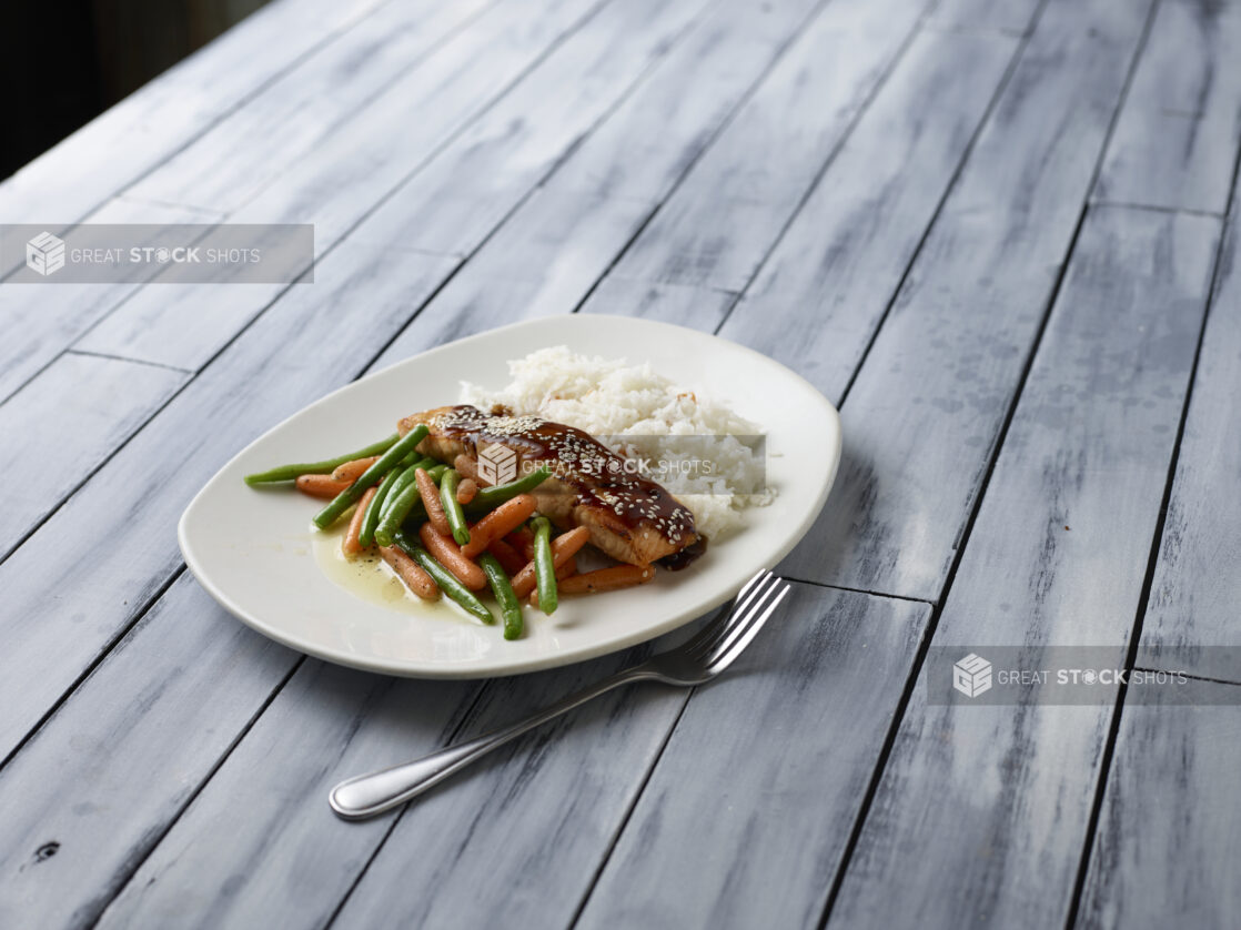 Glazed salmon with buttered vegetables and rice on a wooden background