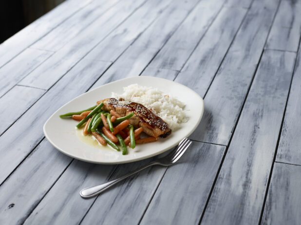 Glazed salmon with buttered vegetables and rice on a wooden background