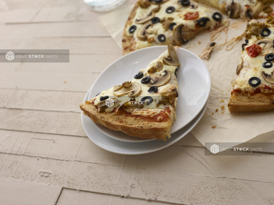 Slice of vegetarian pizza on a plate with other slices in the background on a white wood background