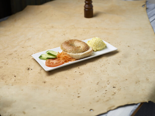 Sesame seed bagel with scoop of egg salad on a white plate