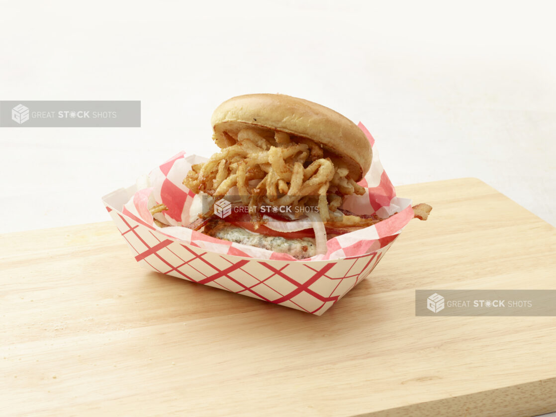 Hamburger with bacon, tomato, cheese and shoestring fried onions with a toasted bun on a cutting board