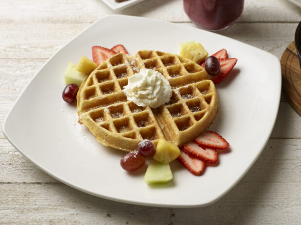 Belgian waffle with fresh fruit and whipped cream on a wooden background
