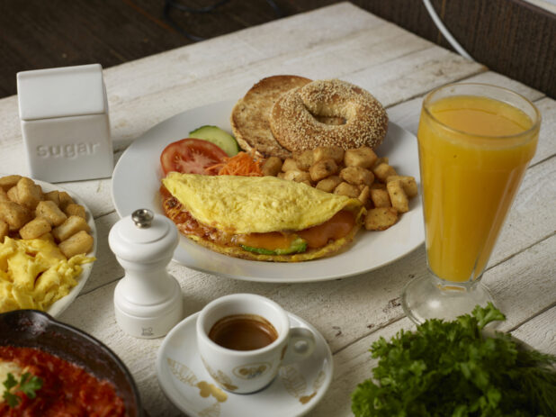 Omelette breakfast plate with a bagel and home fries with espresso and a glass of orange juice on a wooden background