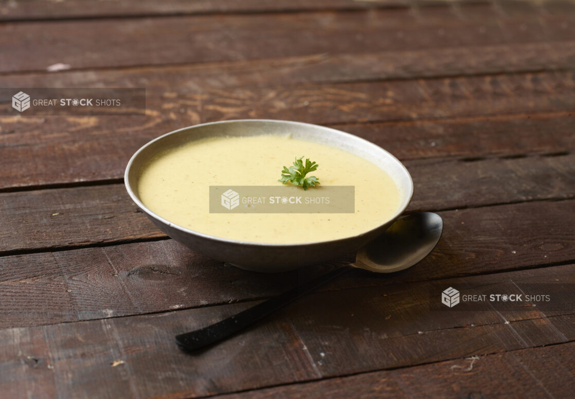 Bowl of cream soup topped with a sprig of parsley on a dark wooden background