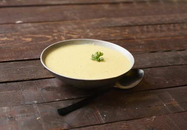 Bowl of cream soup topped with a sprig of parsley on a dark wooden background