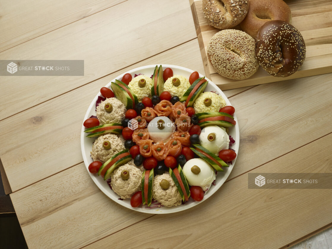 Overhead of various schmears and toppings with bagels in the background on a wooden background