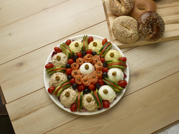 Overhead of various schmears and toppings with bagels in the background on a wooden background