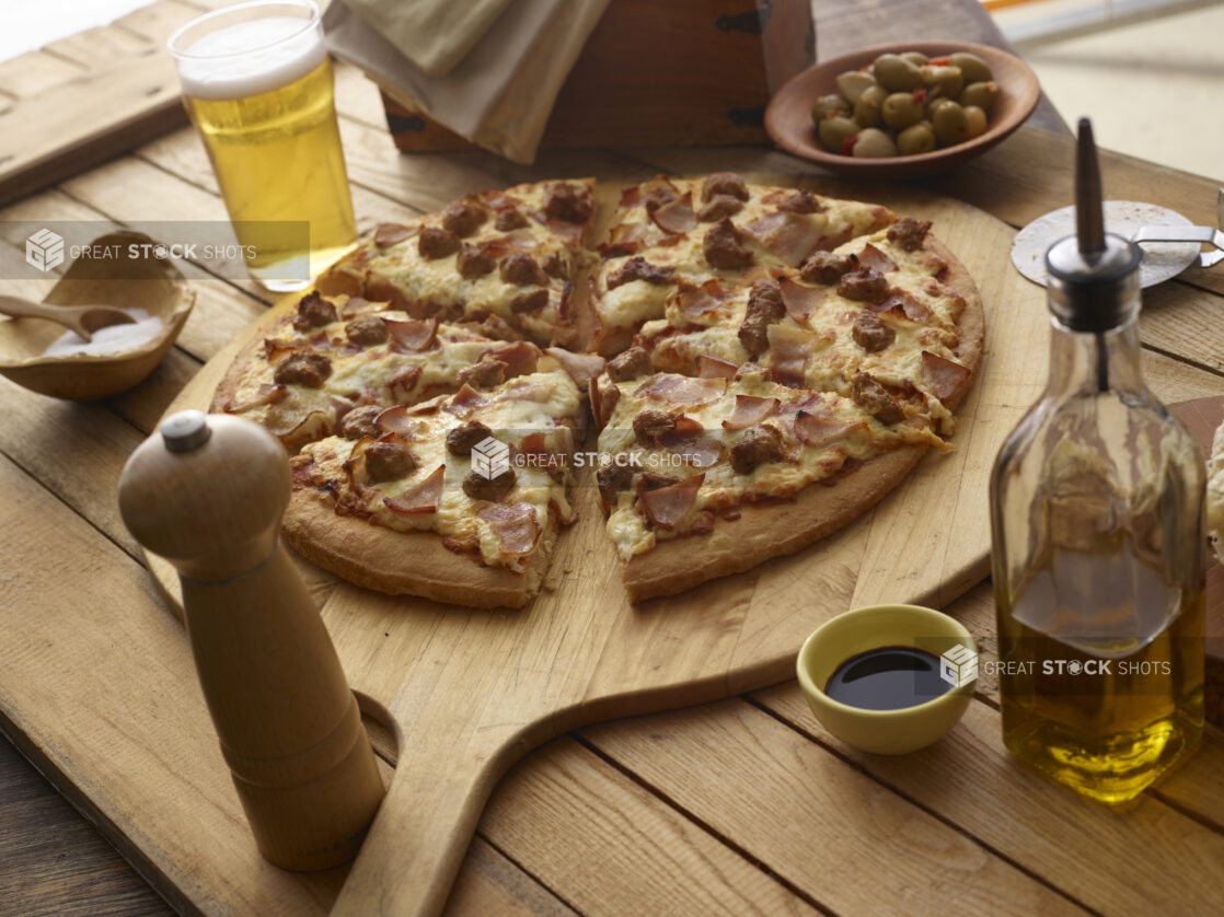 Sliced meat pizza on a pizza paddle with a glass of beer on a wooden background