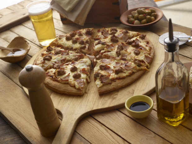 Sliced meat pizza on a pizza paddle with a glass of beer on a wooden background
