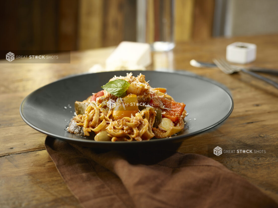 Vegetarian fettuccini in a white bowl in a wooden table with glass of red wine