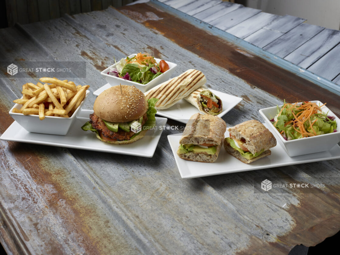 Various vegetarian sandwiches on white plates with a side on a rustic metal background