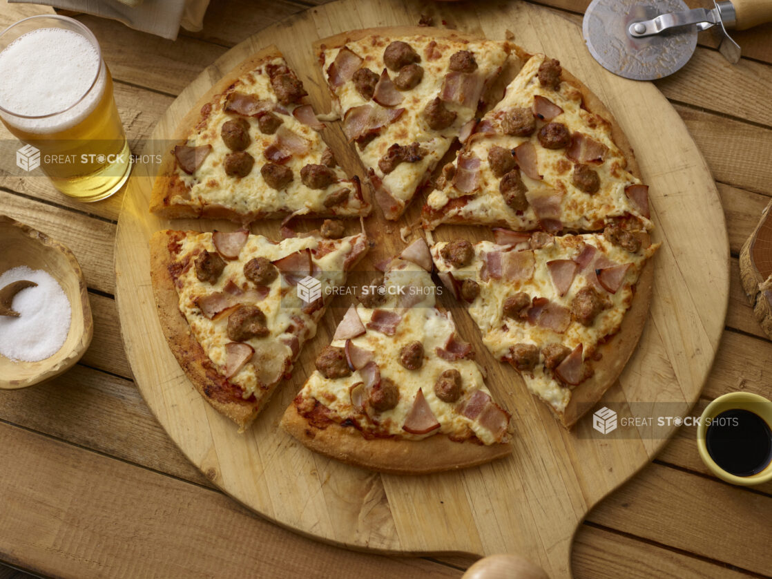 Whole sliced Meat-Lovers-style pizza on a pizza paddle with beer, overhead