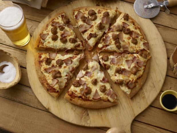Whole sliced Meat-Lovers-style pizza on a pizza paddle with beer, overhead