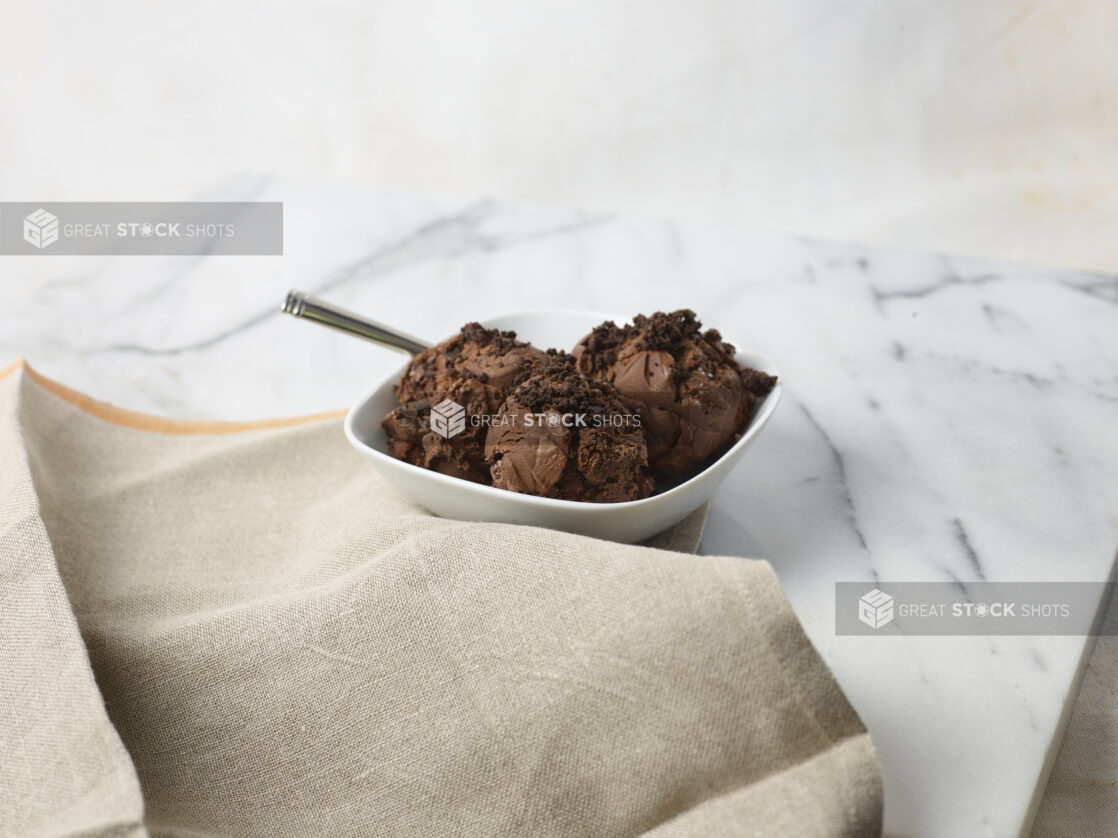 Bowl with three scoops of chocolate ice cream with chocolate cookie crumble on top in a white bowl on a marble background