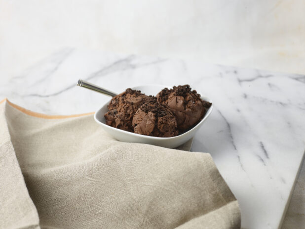 Bowl with three scoops of chocolate ice cream with chocolate cookie crumble on top in a white bowl on a marble background