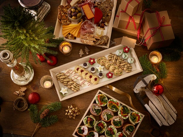 overhead view of charcuterie, cookie and wraps on a wooden platter with holiday decorations