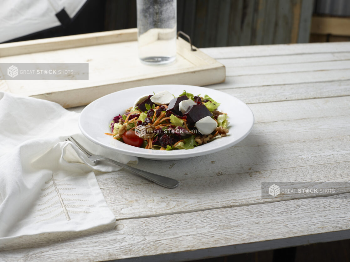 Beet salad in a white bowl on top of a whitewashed wooden background