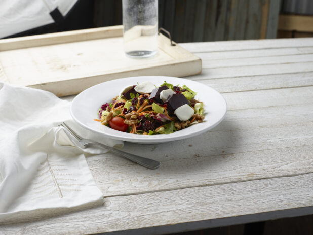 Beet salad in a white bowl on top of a whitewashed wooden background