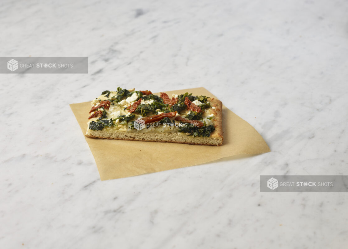 Square slice of California-style vegetarian pizza on parchment paper on top of a marble background