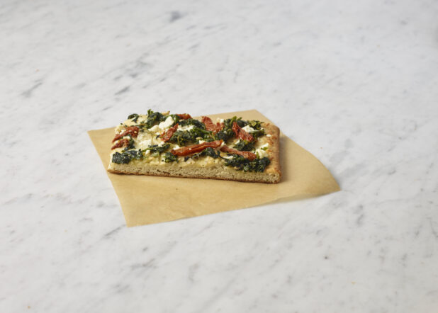 Square slice of California-style vegetarian pizza on parchment paper on top of a marble background