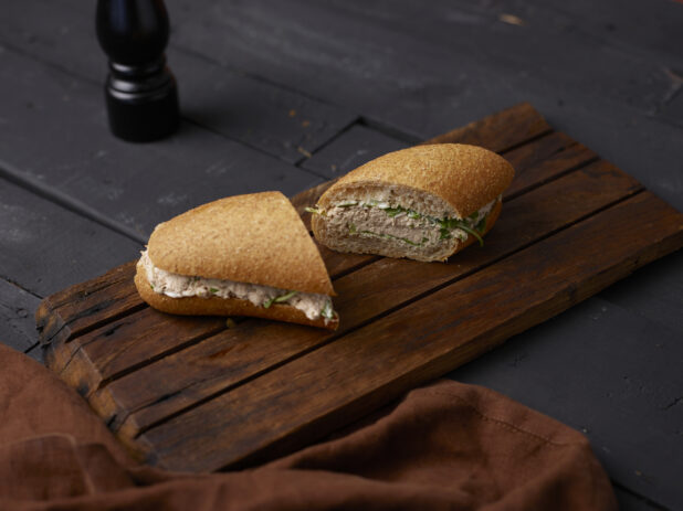 Tuna salad sandwich on a whole grain bun cut in half on a dark wooden board