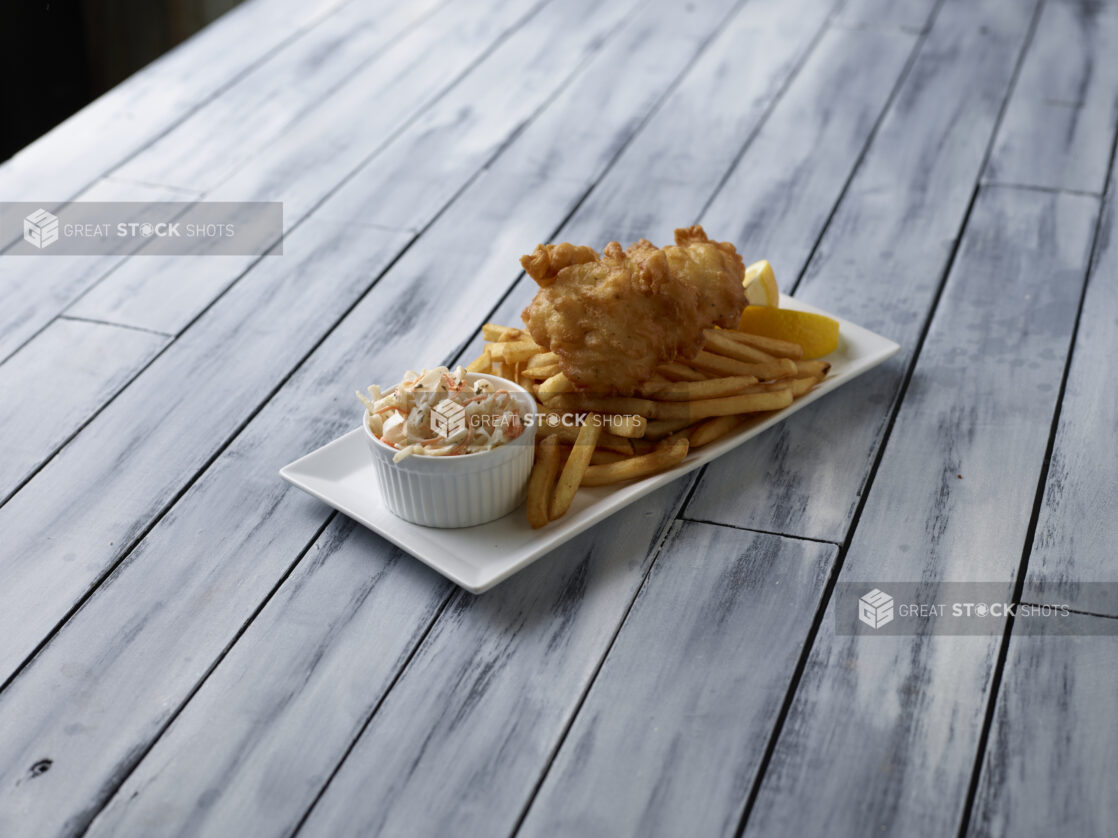 Fish and chips with a side of coleslaw on a wooden background