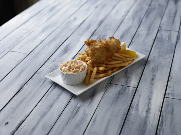 Fish and chips with a side of coleslaw on a wooden background