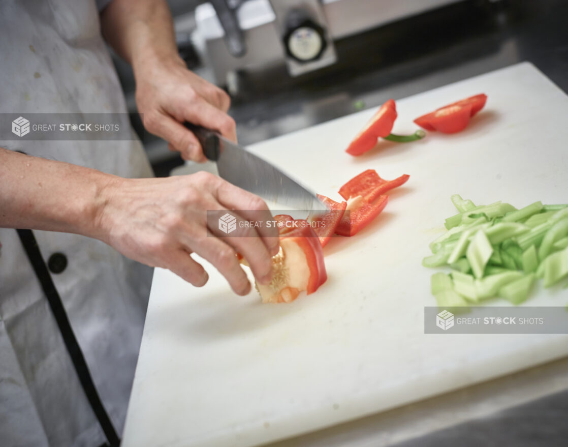 Man in an apron cutting up red pepper on a white cutting board in a restaurant