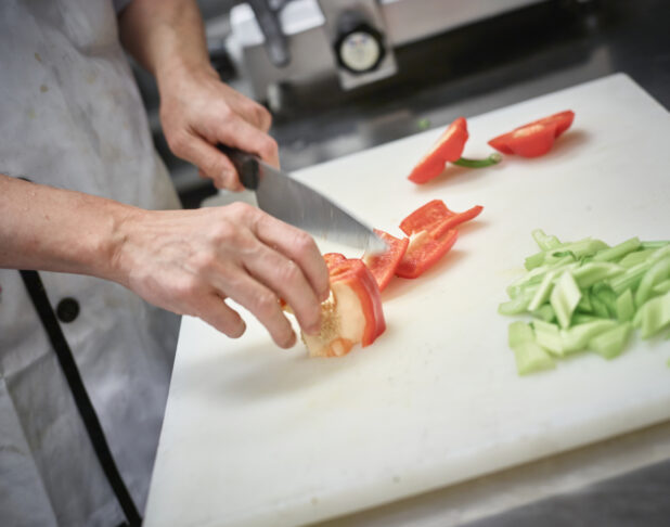 Man in an apron cutting up red pepper on a white cutting board in a restaurant