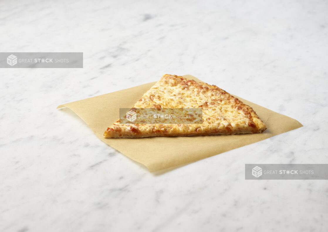 Slice of cheese pizza on parchment paper ontop of a marble background