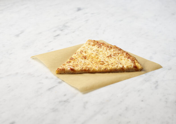 Slice of cheese pizza on parchment paper ontop of a marble background